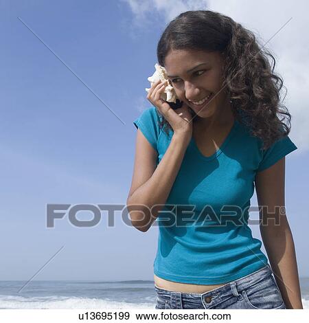 Young woman holding a conch shell close to her ear View Large Photo Image Stock Photo - Young woman holding a conch shell close to her ear. Fotosearch