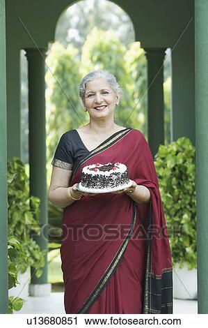 Stock Image - Portrait of a mature woman holding a cake. Fotosearch