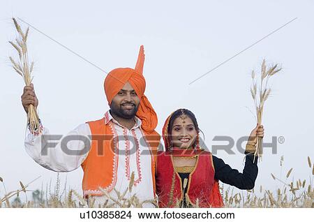 Picture - Portrait of a young couple standing in a wheat field and holding crop. Fotosearch
