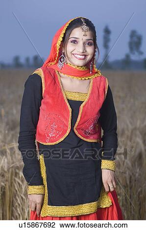 Stock Image - Portrait of a young woman standing in a wheat field and smiling. Fotosearch