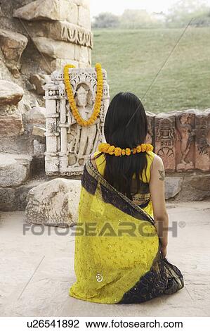 Stock Image - Rear view of a woman kneeling in front of a Hindu idol. Fotosearch