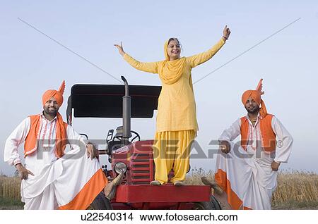 Picture - Young woman with two young men dancing on a tractor. Fotosearch