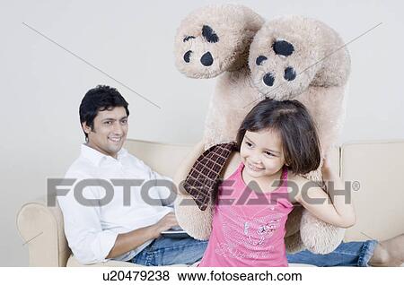 Close-up of a girl holding a teddy bear and her father sitting behind her View Large Photo Image Stock Photo - Close-up of a girl holding a teddy bear and her father sitting behind her. Fotosearch
