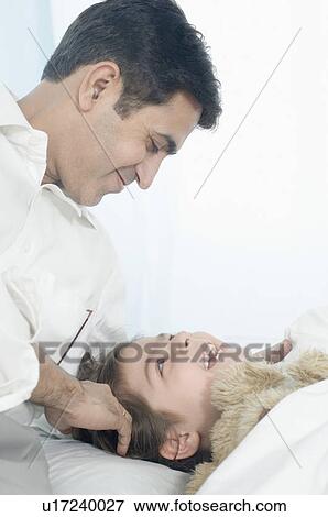 Close-up of a mid adult man looking at his daughter lying on the bed View Large Photo Image Stock Photo - Close-up of a mid adult man looking at his daughter lying on the bed. Fotosearch