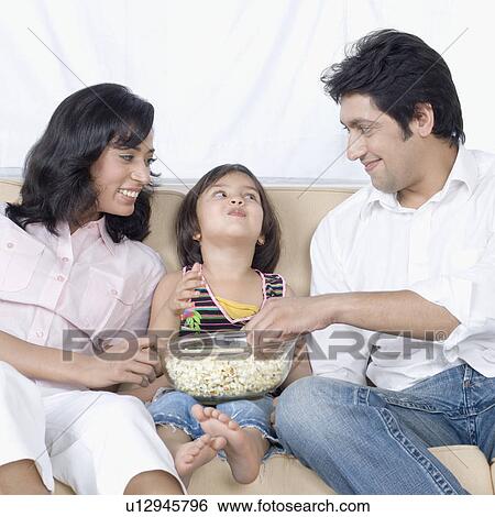 Family sitting on a couch and eating popcorn View Large Photo Image Stock Photograph - Family sitting on a couch and eating popcorn. Fotosearch