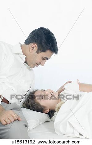 Girl lying on the bed and her father sitting beside her View Large Photo Image Stock Image - Girl lying on the bed and her father sitting beside her. Fotosearch