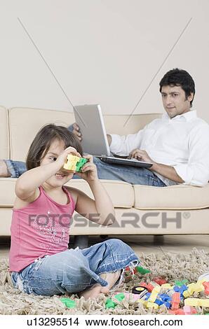 Girl playing with toys with her father sitting behind her and looking at her View Large Photo Image Picture - Girl playing with toys with her father sitting behind her and looking at her. Fotosearch