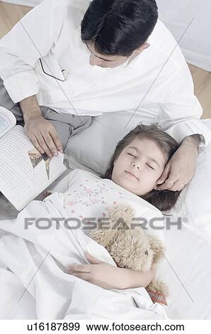 High angle view of a mid adult man reading a book beside his daughter lying on the bed View Large Photo Image Stock Photo - High angle view of a mid adult man reading a book beside his daughter lying on the bed. Fotosearch