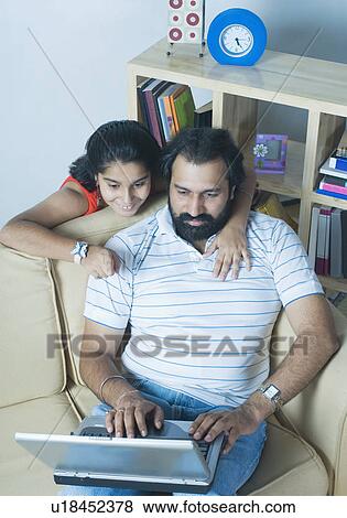 High angle view of a mid adult man using a laptop with his daughter standing behind him View Large Photo Image Stock Photo - High angle view of a mid adult man using a laptop with his daughter standing behind him. Fotosearch