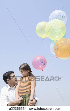 Low angle view of a mid adult man carrying his daughter with balloons View Large Photo Image Picture - Low angle view of a mid adult man carrying his daughter with balloons. Fotosearch