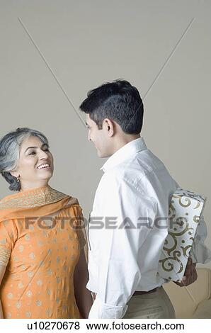 Mature woman standing in front of her son hiding a gift behind his back View Large Photo Image Stock Photo - Mature woman standing in front of her son hiding a gift behind his back. Fotosearch