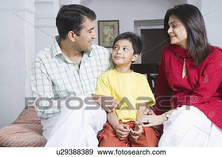 Stock Photo - Mid adult couple sitting with their son and smiling. Fotosearch