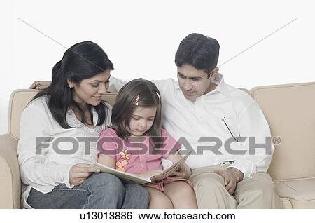 Mid adult couple with their daughter sitting on a couch and reading a book View Large Photo Image Stock Photograph - Mid adult couple with their daughter sitting on a couch and reading a book. Fotosearch