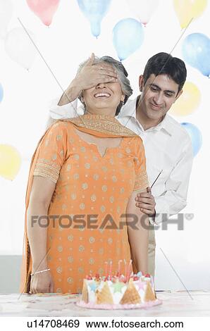 Mid adult man covering eyes of his mother on her birthday View Large Photo Image Stock Photo - Mid adult man covering eyes of his mother on her birthday. Fotosearch