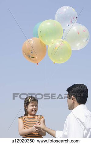 Mid adult man holding balloons with his daughter View Large Photo Image Stock Image - Mid adult man holding balloons with his daughter. Fotosearch