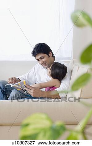 Mid adult man reading a book with his daughter View Large Photo Image Stock Photo - Mid adult man reading a book with his daughter. Fotosearch