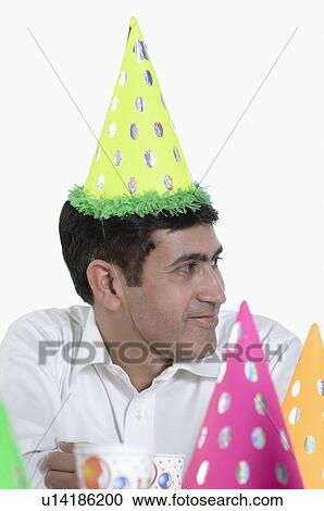 Stock Image - Mid adult man wearing a birthday hat and smiling. Fotosearch