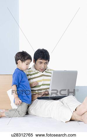 Stock Photography - Mid adult man working on a laptop with his son. Fotosearch