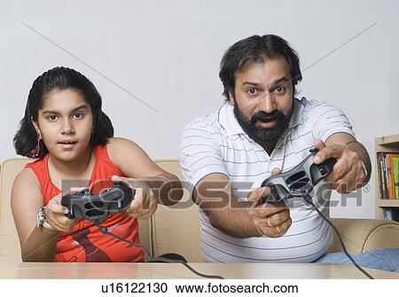 Portrait of a mid adult man sitting on a couch with his daughter and playing video game View Large Photo Image Stock Image - Portrait of a mid adult man sitting on a couch with his daughter and playing video game. Fotosearch