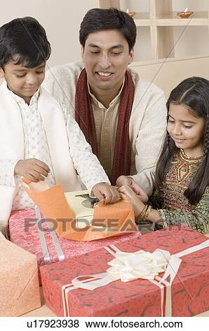 Young man sitting with his children and opening diwali gifts View Large Photo Image Stock Photo - Young man sitting with his children and opening diwali gifts. Fotosearch