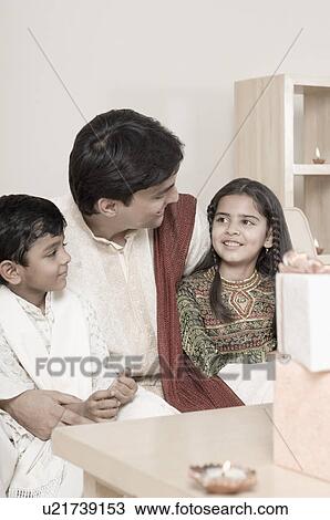 Young man sitting with his son and daughter behind lamps lit on a wooden table View Large Photo Image Stock Image - Young man sitting with his son and daughter behind lamps lit on a wooden table. Fotosearch