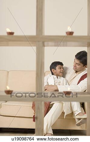 Picture - Young man sitting with his son behind lamps lit on a wooden structure. Fotosearch