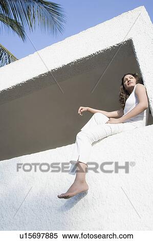 Low angle view of a young woman sitting in the balcony of a building View Large Photo Image Stock Photography - Low angle view of a young woman sitting in the balcony of a building. Fotosearch