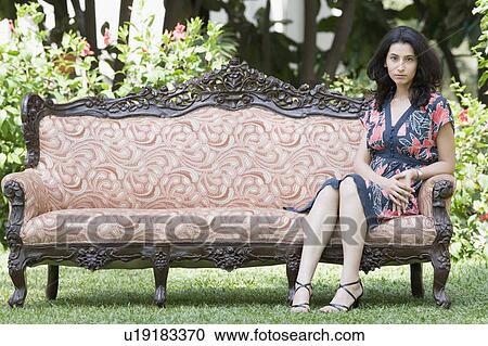 Stock Image - Portrait of a young woman sitting on a couch in a lawn. Fotosearch