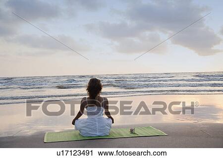 Rear view of a young woman meditating on the beach View Large Photo Image Stock Image - Rear view of a young woman meditating on the beach. Fotosearch