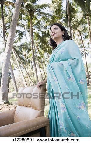 Stock Image - Side profile of a mature woman standing near an armchair. Fotosearch