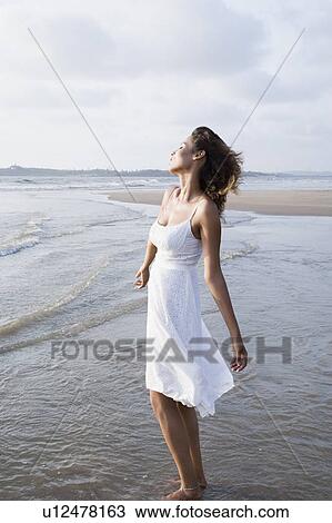 Side profile of a young woman standing on the beach with her eyes closed View Large Photo Image Stock Image - Side profile of a young woman standing on the beach with her eyes closed. Fotosearch