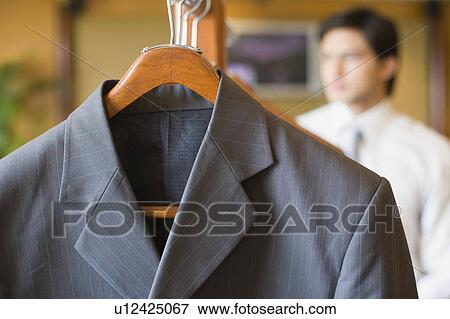 Stock Photo - Close-up of a business suit hanging on a clothes rack with a businessman in the background. Fotosearch