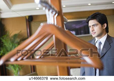 Close-up of hangers hanging on a clothes rack with a businessman standing in the background View Large Photo Image Stock Photo - Close-up of hangers hanging on a clothes rack with a businessman standing in the background. Fotosearch