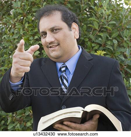 Portrait of a mature man holding a book and pointing forward View Large Photo Image Stock Image - Portrait of a mature man holding a book and pointing forward. Fotosearch