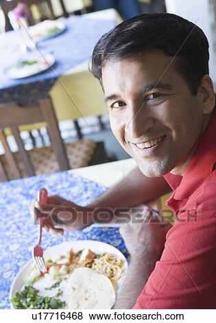 Portrait of a mid adult man eating food in a restaurant View Large Photo Image Stock Photo - Portrait of a mid adult man eating food in a restaurant. Fotosearch