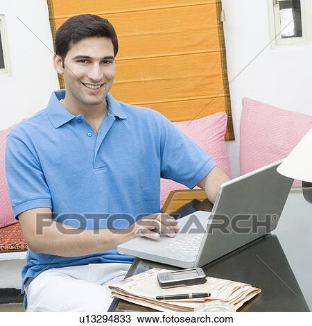 Portrait of a young man working on a laptop and smiling View Large Photo Image Stock Image - Portrait of a young man working on a laptop and smiling. Fotosearch