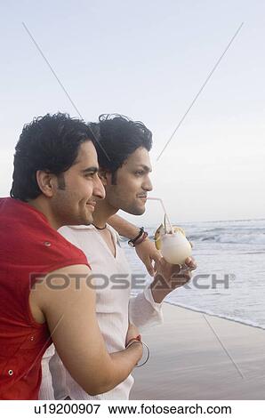 Side profile of a young man hugging his friend drinking cocktail on the beach View Large Photo Image Stock Photo - Side profile of a young man hugging his friend drinking cocktail on the beach. Fotosearch