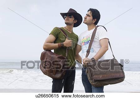 Stock Photography - Two young men standing on the beach with their arms around each other. Fotosearch