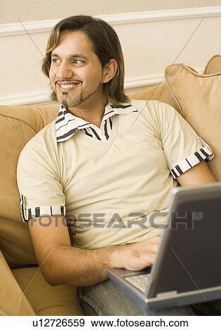 Young man using a laptop on a couch View Large Photo Image Stock Photo - Young man using a laptop on a couch. Fotosearch