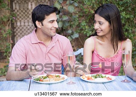 Stock Photo - Close-up of a young couple sitting at a dining table and eating food. Fotosearch