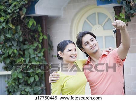 Stock Photography - Close-up of a young man holding a key with his wife beside him. Fotosearch