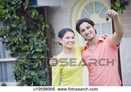 Stock Photograph - Close-up of a young man holding the key of his new house with his wife beside him. Fotosearch