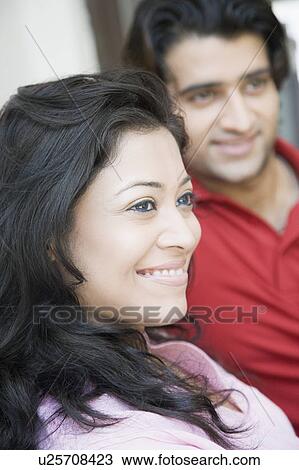 Stock Image - Close-up of a young woman smiling with a young man sitting beside her. Fotosearch