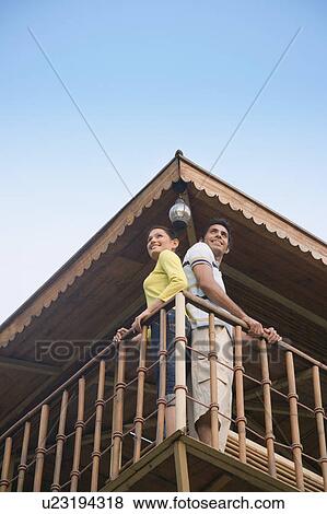 Stock Photo - Low angle view of a young couple standing at the railing of a log cabin and smiling. Fotosearch