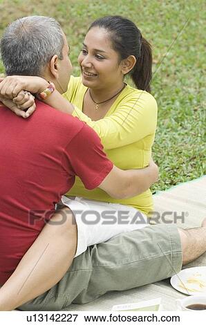 Stock Photo - Mid adult couple sitting in a park and embracing each other. Fotosearch