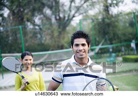 Portrait of a young couple standing in a tennis court and smiling View Large Photo Image Stock Image - Portrait of a young couple standing in a tennis court and smiling. Fotosearch
