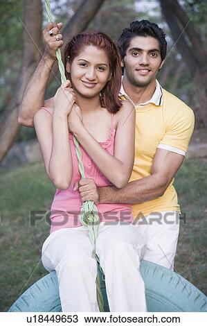 Stock Image - Portrait of a young couple swinging on a swing and smiling. Fotosearch
