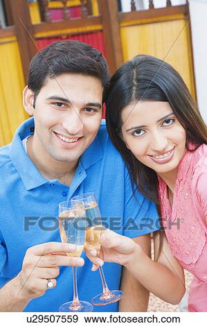 Stock Photo - Portrait of a young couple toasting with champagne flutes and smiling. Fotosearch