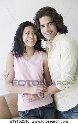 Stock Photograph - Portrait of a young man standing with his arm around a young woman and smiling. Fotosearch