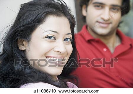 Portrait of a young woman smiling with her husband in the background View Large Photo Image Stock Image - Portrait of a young woman smiling with her husband in the background. Fotosearch